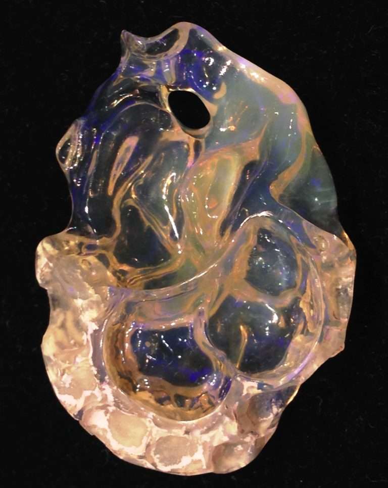 Honey opal carving with clay left at the base to frame the stone. Purple hues seen throughout the stone.